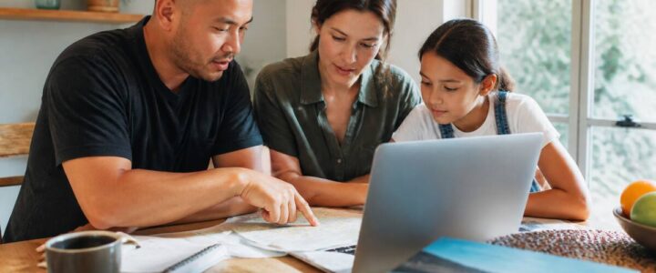 Gezin dat in huis aan een tafel reizen en vakanties vergelijkt op laptop en met reisnotities