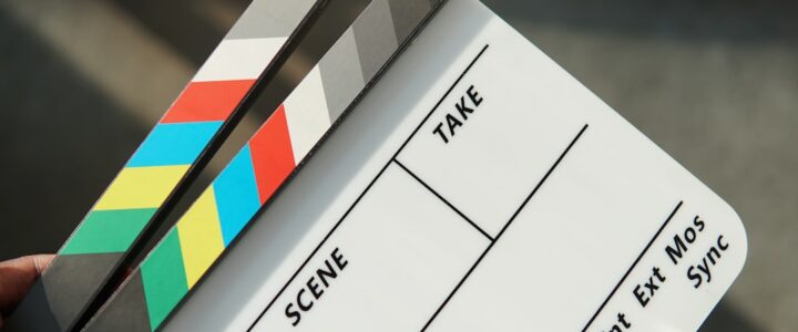 A person holding a movie clapper and a pair of scissors